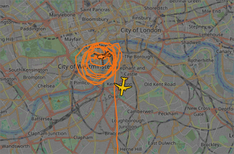 Flight radar map showing central London with two planes. One plane is flying in a circular holding pattern over the city, indicated by an orange line, while the other plane is flying southward along a straight path.