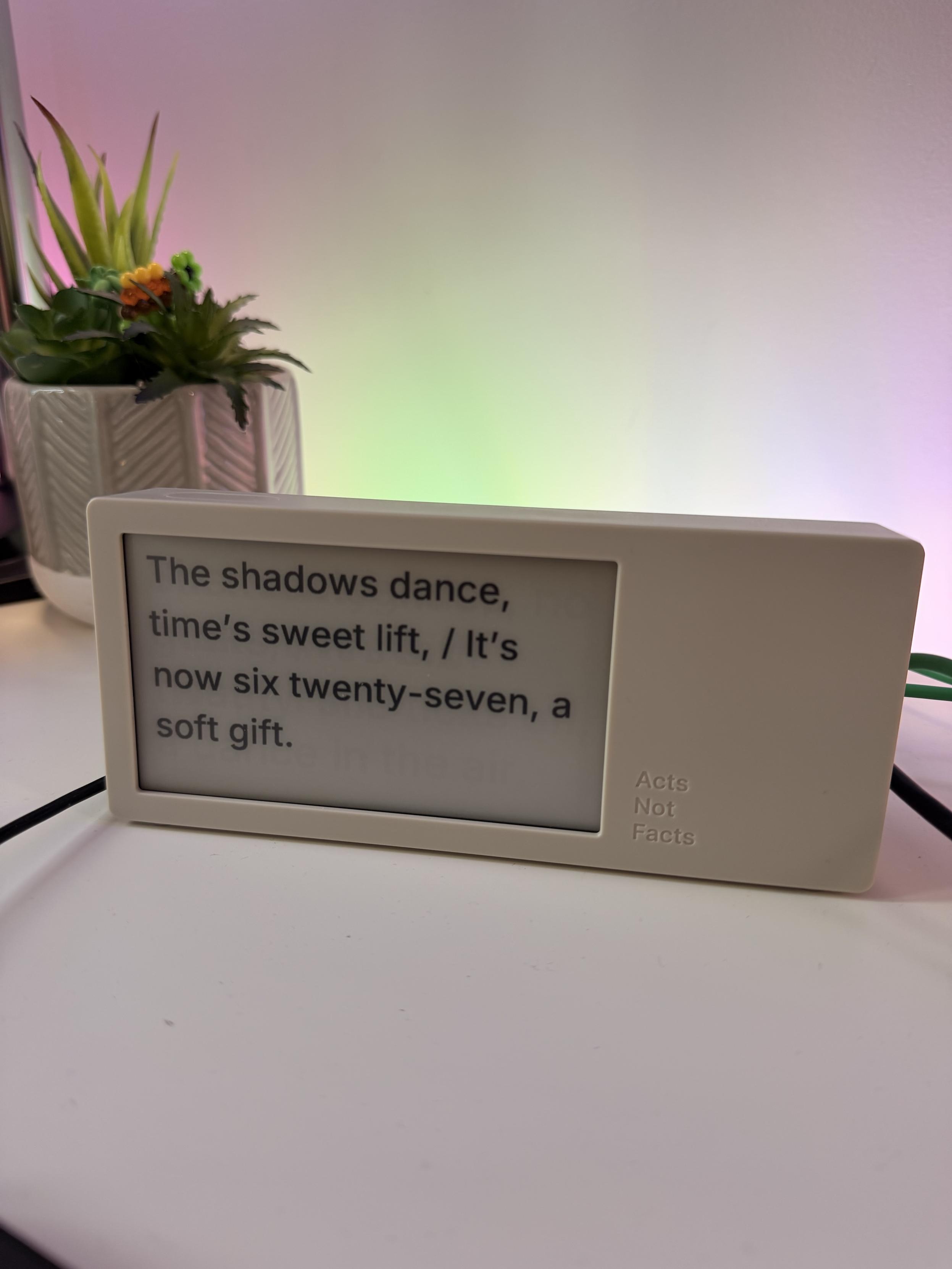 The image features a small digital display showing a poem or phrase that reads: "The shadows dance, time’s sweet lift, / It’s now six twenty-seven, a soft gift." A potted plant with colorful succulents is visible in the